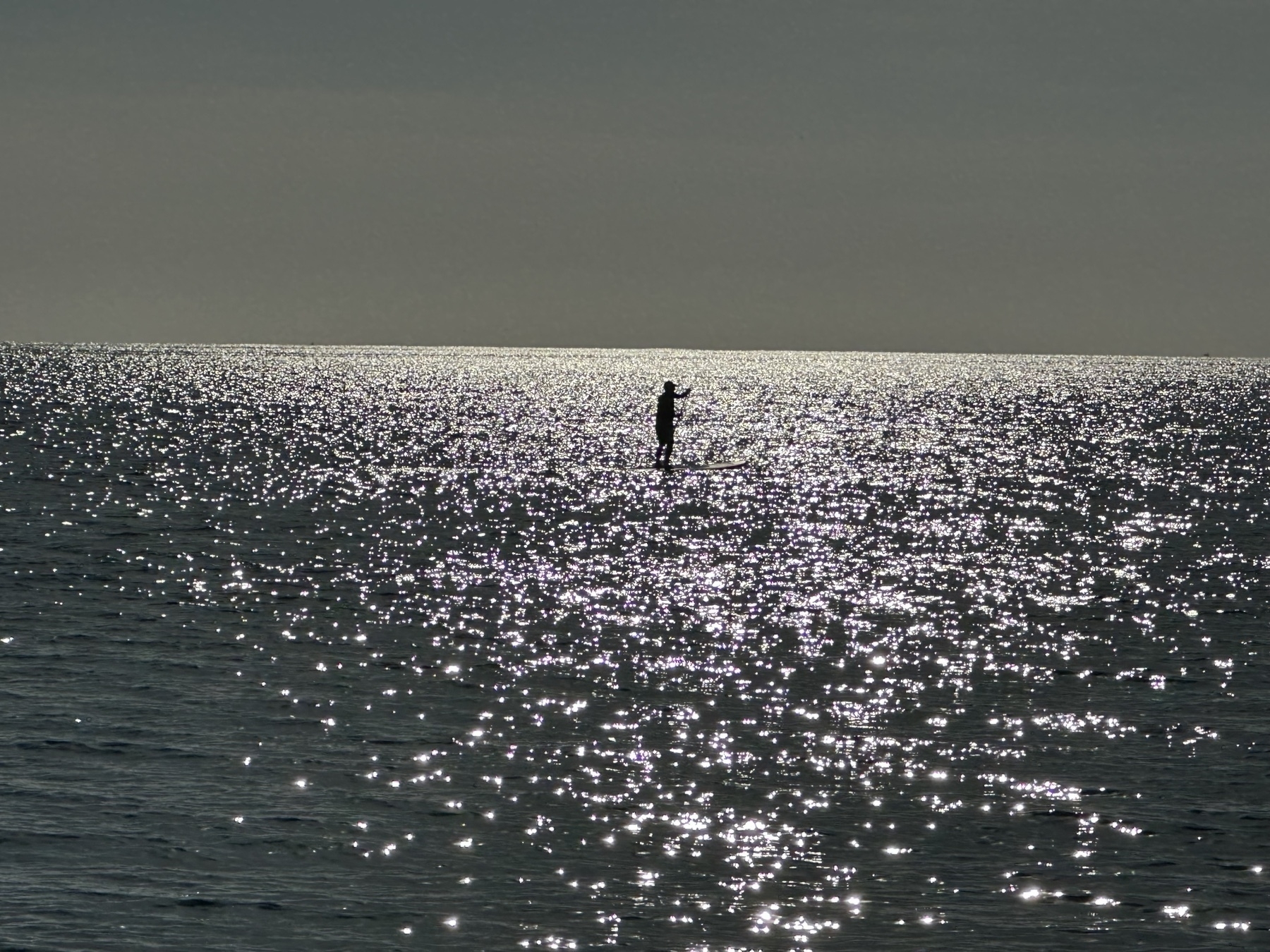 Person standing on a paddle board on a calm sea, wifh the sun rising behind. 